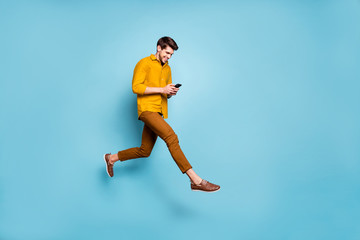 Fototapeta na wymiar Full length profile photo of funny guy jumping high holding telephone millennial writing email walking down street wear yellow shirt pants isolated blue color background