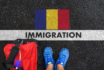 Man in shoes with bag standing next to line with word IMMIGRATION and flag of Romania on asphalt...