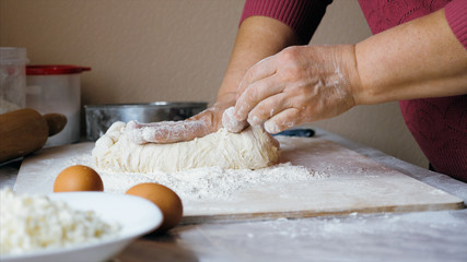 Close-up hands of senior female is kneading a dough in flour on the table at home kitchen, side view