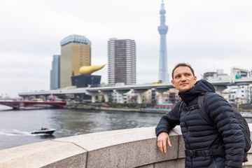 Tokyo, Japan Sumida area cityscape skyline and river in downtown on cloudy day with boat swimming and young tourist man on bridge