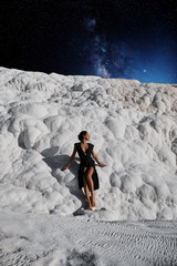 Surrealistic photo of a young beautiful girl in a black dress standing by the Pamukkale natural pool with space in the background