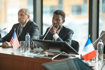 African young businessman and senior businessman sitting at the table and listening at conference
