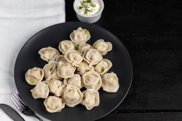 Boiled dumplings. In the background are greens, red peppers and bay leaves. On a black wooden background with a white napkin.