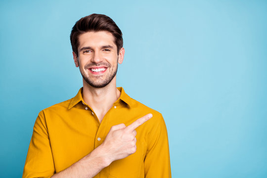 Photo of handsome cheerful attractive beaming man pointing at empty space with forefinger smiling toothily isolated over blue pastel color background