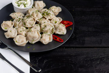 Boiled dumplings. In the background are greens, red peppers and bay leaves. On a black wooden background with a white napkin.