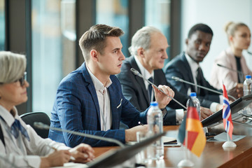 Young businessman sitting at the table and speaking the speech during debates with other political leaders