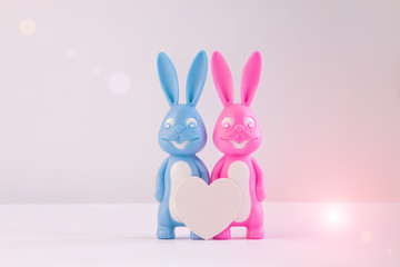 Valentine's day card, cute bunnies happy lovers couple with white heart on light bokeh background. Family love and dating concept.Easter banner. Pink and blue rabbits.Creative minimal style,copy space
