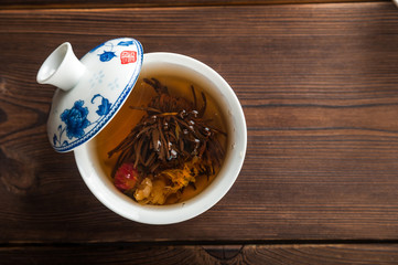 Knitted blooming tea in a porcelain teapot close-up. Tea ceremony on a dark wooden background and copy space.