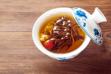 Knitted blooming tea in a porcelain teapot close-up. Tea ceremony on a dark wooden background and copy space.
