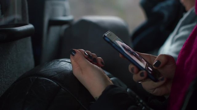 A girl photographs nails on a smartphone while sitting in a passenger seat bus.