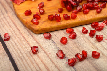 Pieces of ripe juicy pomegranate and pomegranate seeds on a wooden Board on a wooden background. Close up.