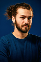 Obraz premium Portrait of gorgeous caucasian bearded hipster in blue shirt standing in front of blue background and having serious facial expression.