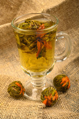 Flower tea brewed in a glass Cup and balls of flower tea on a background of rough homespun fabric. Close up.