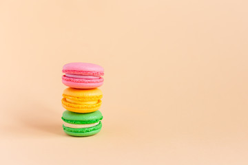 Three tasty french macarons on peach pastel background.  Pink, yellow and green macarons.