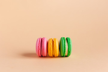 Three tasty french macarons on peach pastel background.  Pink, yellow and green macarons.