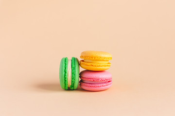 Three tasty french macarons on peach pastel background.  Pink, yellow and green macarons.