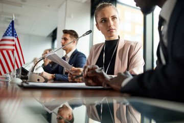 Young businesswoman sitting at the table with report and discussing it with her colleague at...