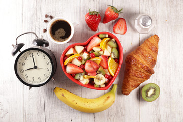 alarm clock with fruit salad, croissant and coffee cup