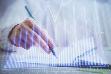 Financial forex graph displayed on hands taking notes background. Concept of research. Double exposure
