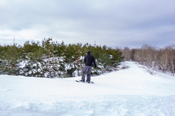 Naklejka na ściany i meble A man on a cloudy winter day rolls along the side of a mountain on a snowboard.