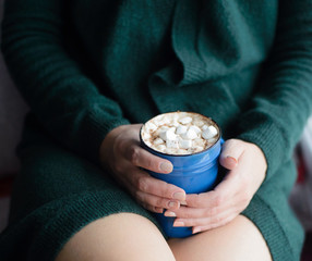 white caucasian woman in green knitted cardigan holding blue cup with cacao and marshmallow, front view, vertical stock photo image