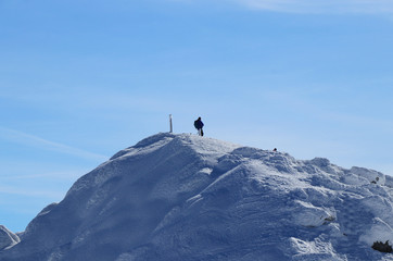 Naklejka na ściany i meble Lone wolf on the peak of Chopok in Low Tatras in Slovakia, Europe. Snowy hill and man with rucksak stands and enjoy views to the valley and paradise blue sky. Concept of wildness and freedom