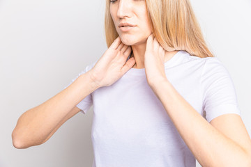 Female checking thyroid gland by herself. Close up of woman in white t- shirt touching neck with...