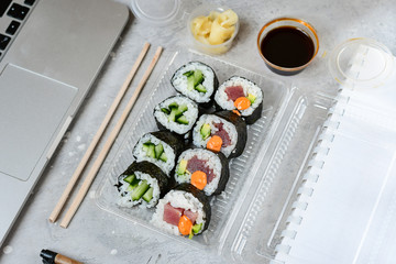 Food delivery concept. Lunch box with sushi set food delivery. Top view of assorted sushi, uramaki, hosomaki and nigiri. on grey office table. Lunch at the office. Top view , flat lay food, Takeaway,