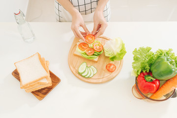 Women are making vegetarian sandwiches with lettuce, cucumber, tomatoes, water on the table in the modern kitchen.