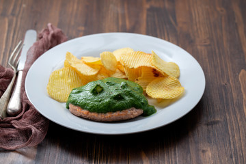 grilled hamburger with green sauce nd potato chips on white plate