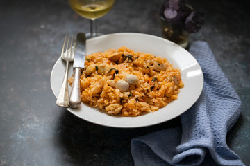 rice with seafood on white plate and glass of white wine
