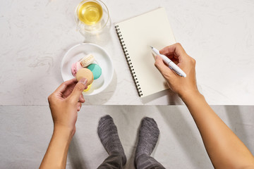 Man writing on notebook and eating cake macaron with tea mug on white background. Top view