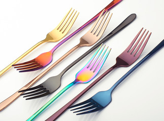 multi-colored metal forks on a white background, cutlery