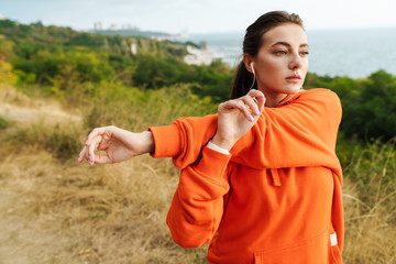 Photo of athletic woman stretching her arms and using earphones