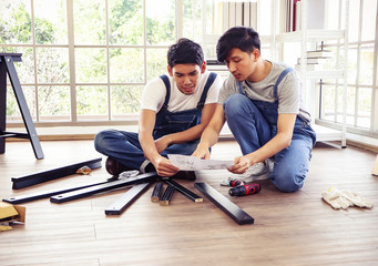 Two  Asian men trying to assemble knockdown furniture and getting confused. - obrazy, fototapety, plakaty
