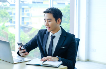 Young businessman sitting and working on desk and using smart phone connecting internet and documents at office, employee or company ceo using online apps software at workplace