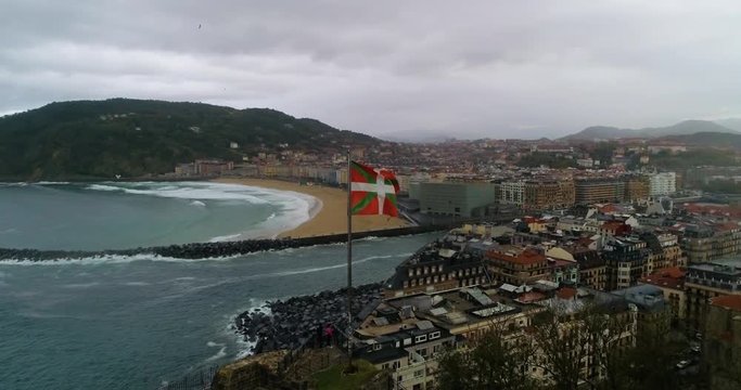 Drone orbiting view of San Sebastian with Basque Flag flapping in foreground.