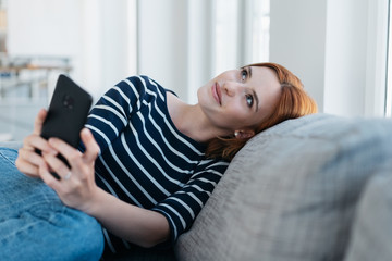 Happy young woman sitting daydreaming on a sofa