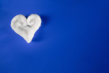 Handmade white cotton heart on blue paper background. Space copy. Flat lay.