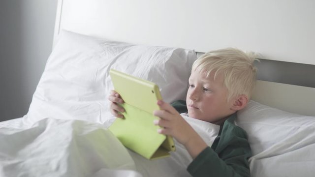 handsom blonde Boy Plays a Game on a Tablet in the morning in bed