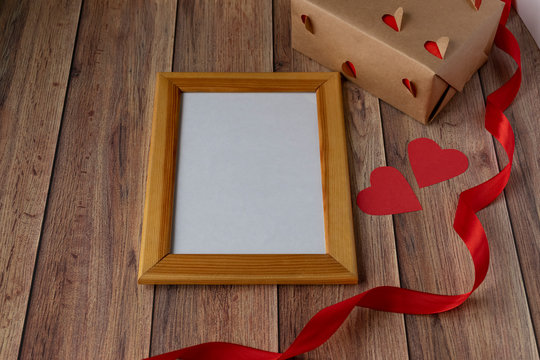 Valentine's day background. Photo frame, gift, heart and red satin ribbon on a wooden background. Valentine's Day, Mother's Day..