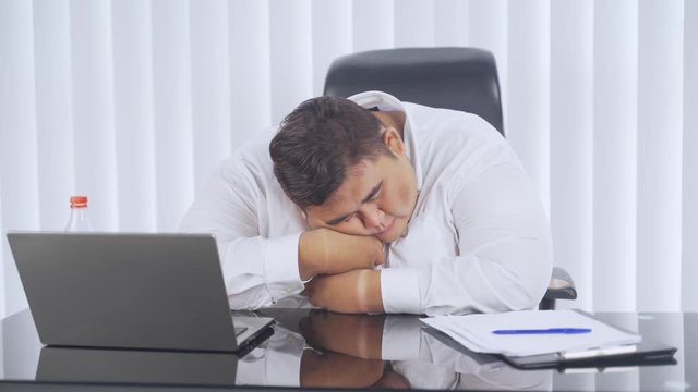 Overweight businessman sleeping on desk in the office room with a laptop on the table. Shot in 4k resolution