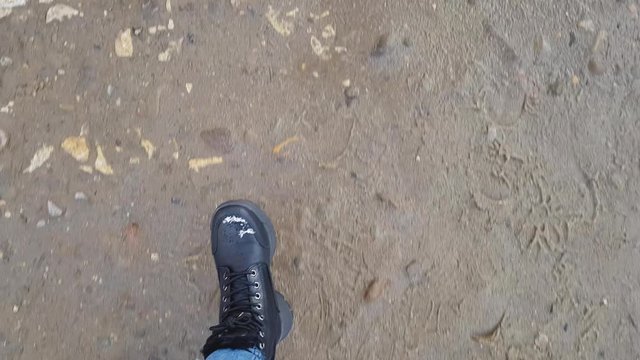 A view from above on the legs in jeans and black boots, which walk along the gravel road to Aushvice, first-person view, POV
