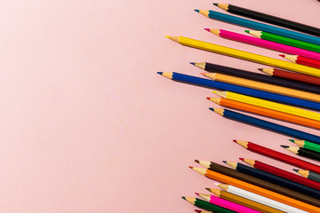 Scattered colored pencils of different lengths on a pink background on the right side, tending to the center. Horizontal close-up
