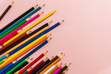 Scattered colored pencils of different lengths on a pink background with a left corner, tending to the center. Horizontal close-up