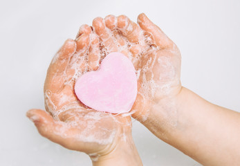 Importance of personal hygiene care. Flat lay view of child washing dirty hands with pink heart shape soap bar, lot of foam. Copy space. - obrazy, fototapety, plakaty