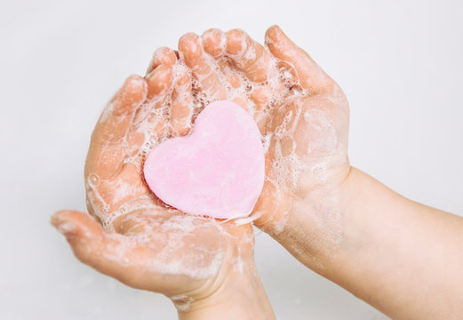 Importance of personal hygiene care. Flat lay view of child washing dirty hands with pink heart shape soap bar, lot of foam. Copy space. - Powered by Adobe