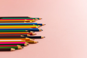 Colored pencils of different lengths are scattered, extending into the distance, on a pink background on the left side, tending to the center. Horizontal side view