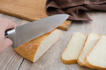 long loaf on a wooden board and knife. Delicious Ukrainian bread. Hand cuts a knife with white bread, close-up ..
