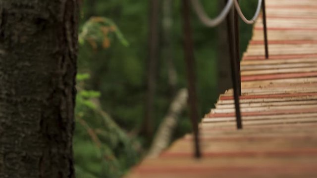 Close up of the edge of hanging wooden bridge on blurred green grass background. Stock footage. Wobbling wooden suspension bridge in city park.